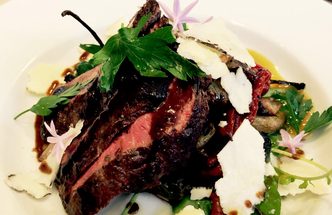 Oak Avenue Catering’s roasted American Akaushi tenderloin accompanied by braised greens, Italian parsley, roasted Jimmy Nardello peppers, shaved pecorino, society garlic blooms, and marchand de vin. 